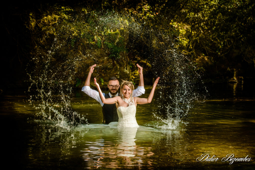 photo en couleur d'un couple de jeune marié pendant une séance trash the dress ils sont debout dans l'eau d'une rivière proche de la ville de Decazeville en Aveyron ils sont heuruex et jete de l'eau par dessus leurs têtes