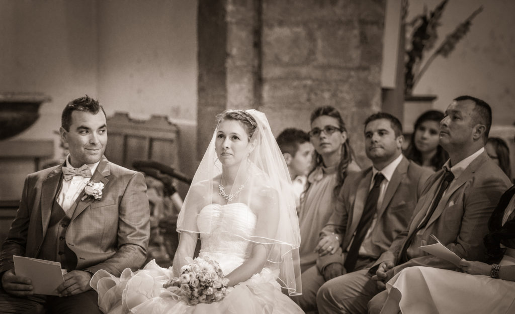 photo de mariage en sépia à l'intérieur de l'église de Bozouls en Aveyron la mariée a un songeur et le marié a un regard plein de tendresse la photographie a été prise en lumière ambiante par le photographe de Rodez Didier Bezombes